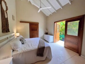 A bedroom with a bed, a nightstand, a dresser, a ceiling fan, and a sliding glass door leading to a garden. - Casa Ola, Lux 5 Bedrm, 5 Bath Villa, w' Private Pool, 2 min walk to Playa Coson (Las Terrenas)