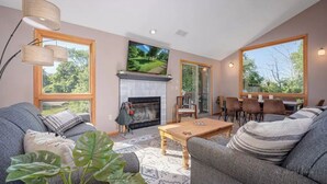 Un salon chaleureux avec une cheminée, des sièges confortables et de grandes fenêtres donnant sur l’extérieur.