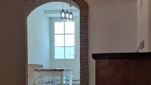 Una habitación amplia con suelo de madera, un arco de ladrillo que da a un comedor con mesa y sillas, y un armario de madera.