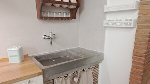 Una cocina con un lavamanos de piedra, estantes de madera y una pared de ladrillo.