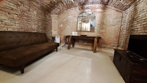 Una habitación con pared de ladrillo, un banco de madera, un sofá, una mesita con espejo y un televisor.