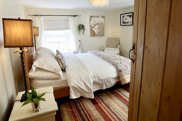 Een slaapkamer met een bed, een nachtkastje met lamp, een stoel en een raam met gordijnen.