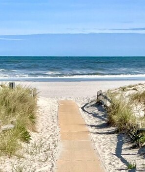 A sandy beach path leading to the ocean with grassy dunes on either side.
