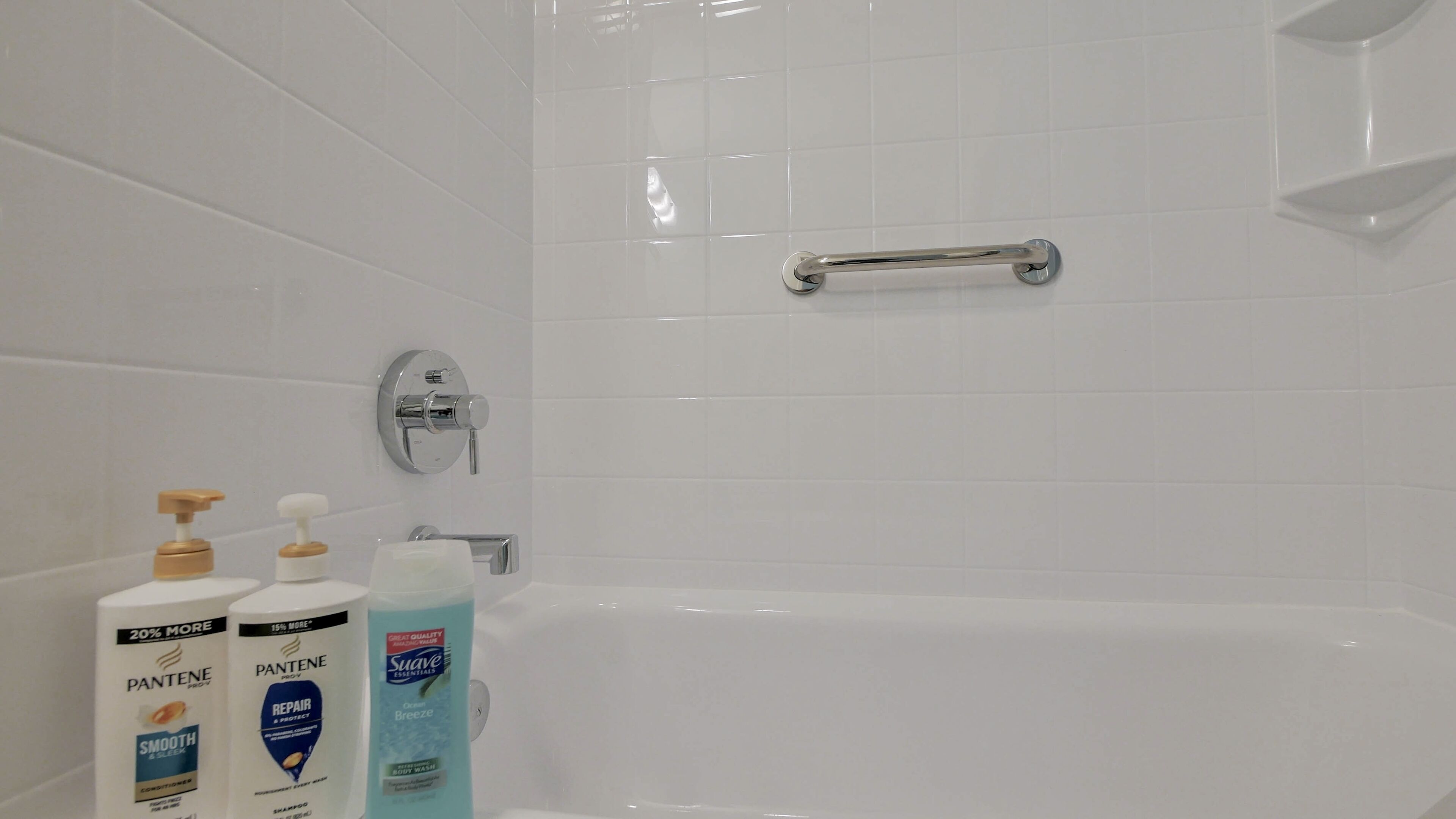 A bathroom with a bathtub, a handrail, and toiletries including Pantene and Suave products.