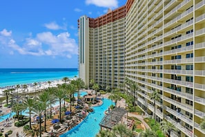 Un hotel de gran altura con zona de piscina, vista a la playa y varios balcones.