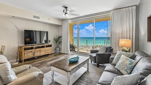 A living room with a television, sofa, coffee table, and a view of the beach. - Shores of Panama 719 - Spacious 7th Flr 2 BR Plus Bunks/3 BA with Parking (Panama City Beach)