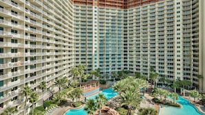 A high-rise hotel with multiple balconies, a central swimming pool, and surrounding palm trees. - Shores of Panama 719 - Spacious 7th Flr 2 BR Plus Bunks/3 BA with Parking (Panama City Beach)