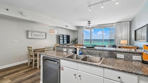 A modern kitchen with granite countertops, stainless steel appliances, and a view of the ocean. - Shores of Panama 719 - Spacious 7th Flr 2 BR Plus Bunks/3 BA with Parking (Panama City Beach)
