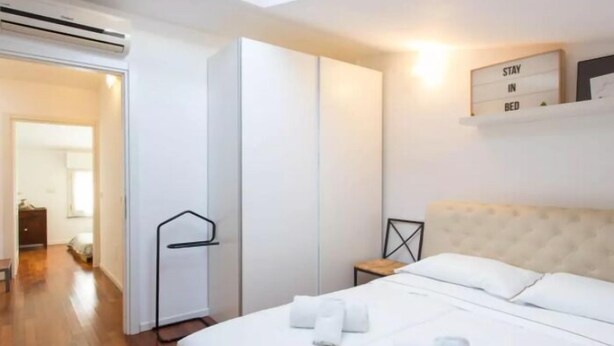 A modern hotel room with a bed, a wardrobe, a small table, and a wall-mounted shelf with a motivational sign. - VALSUGANA (Milan)