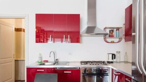 A modern kitchen with red cabinets, stainless steel appliances, and a black dining table. - VALSUGANA (Milan)