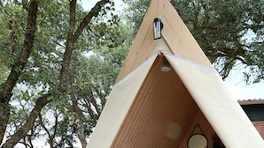 A wooden tent with a bed and a small table, surrounded by trees. - Natura Fun House & Camping (Sintra)