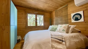 A wooden cabin bedroom with a bed, pillows, a window, and a framed picture on the wall. - Natura Fun House & Camping (Sintra)