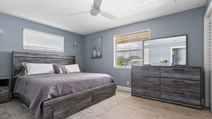 A bedroom with a bed, nightstands, a dresser, a ceiling fan, and a window with blinds.