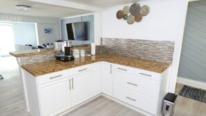 A modern kitchen with white cabinetry, granite countertops, and a tiled backsplash.