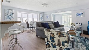 A modern living room with a grey sofa, a floral armchair, and a bar area with white bar stools.