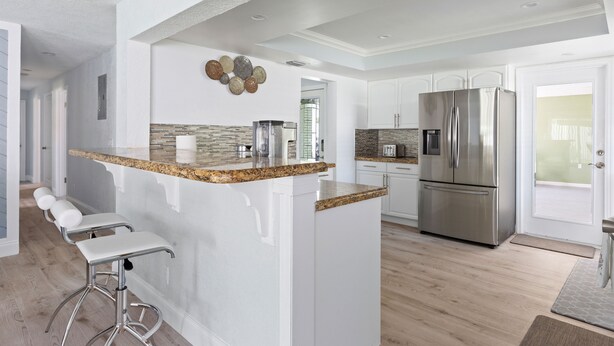 A modern kitchen with a central island, bar stools, stainless steel appliances, and a decorative wall piece.