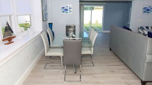 A modern dining area with a glass table and chairs, a sofa, and a view of the outdoors.