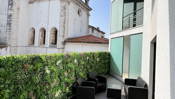 Un balcon doté d’un plancher en bois foncé, de mobilier d’extérieur noir et d’une haie verte.