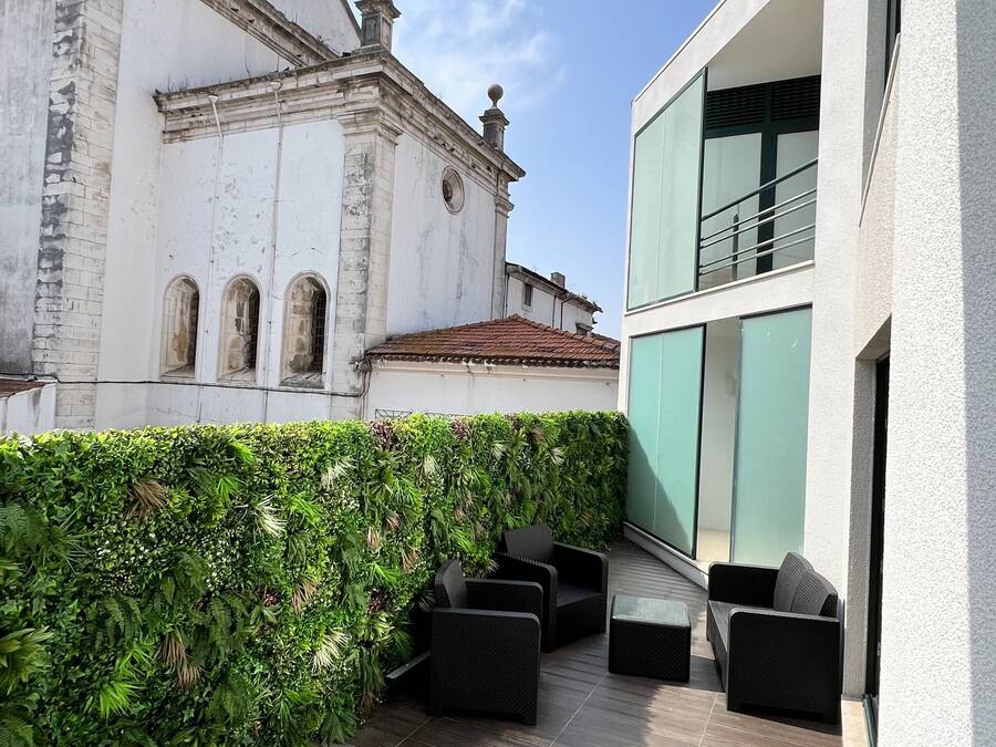 A balcony with dark wooden flooring, black outdoor furniture, and a green hedge.