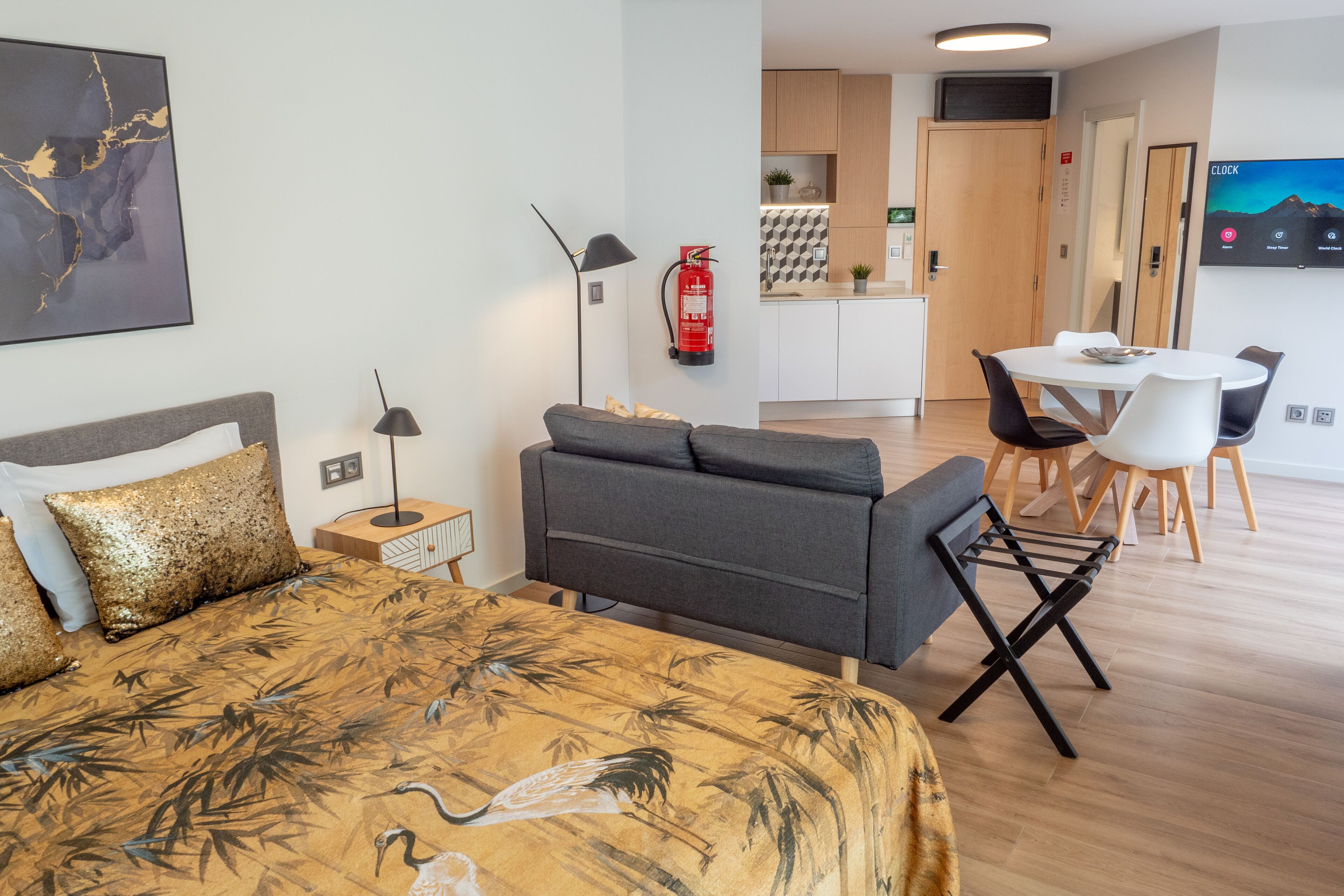 Een hotelkamer met een bed, een bank, een eettafel met stoelen, een keukenhoek en een wandtelevisie.