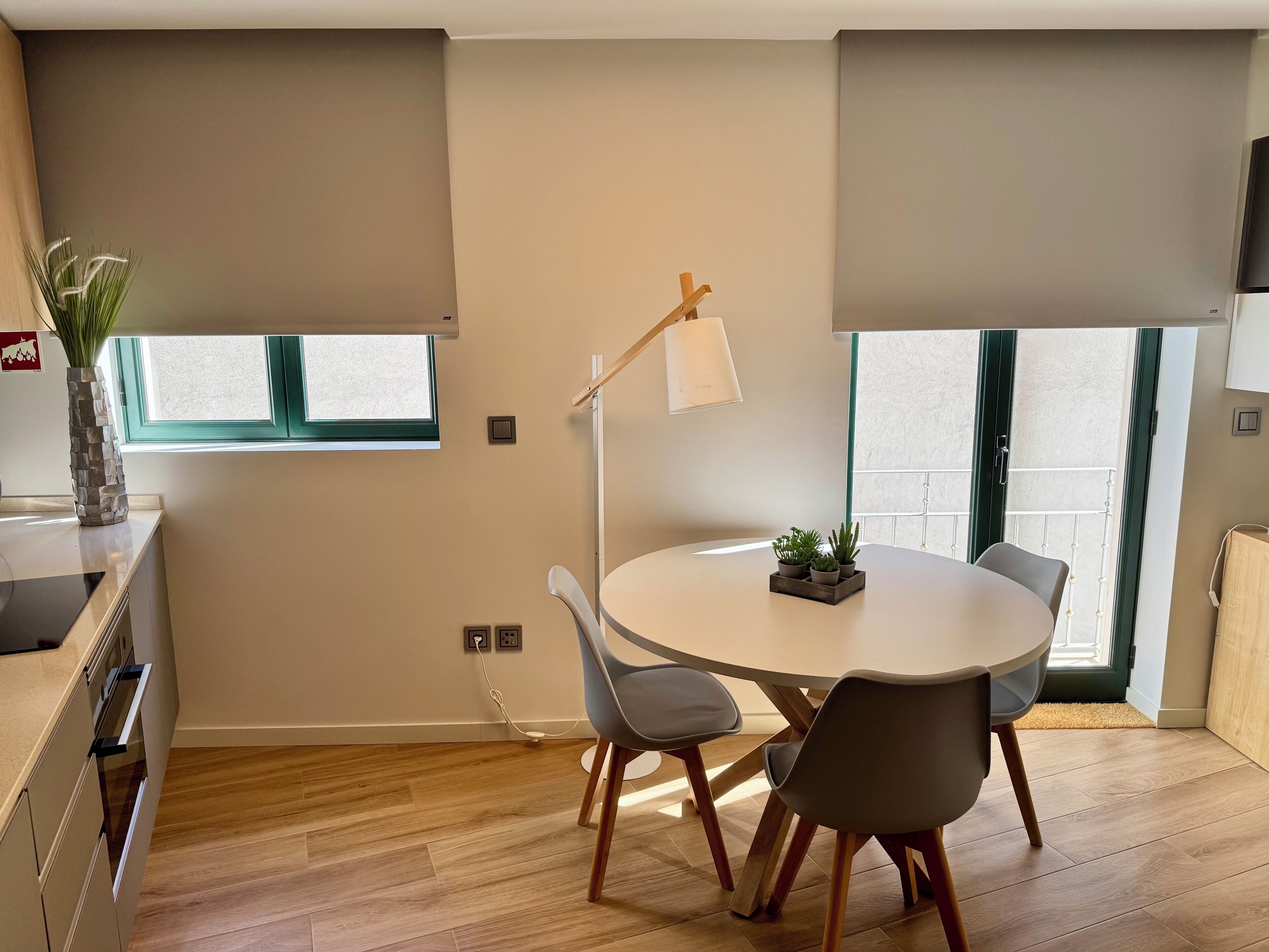 A modern kitchen with a dining area, wooden flooring, and a window providing natural light.