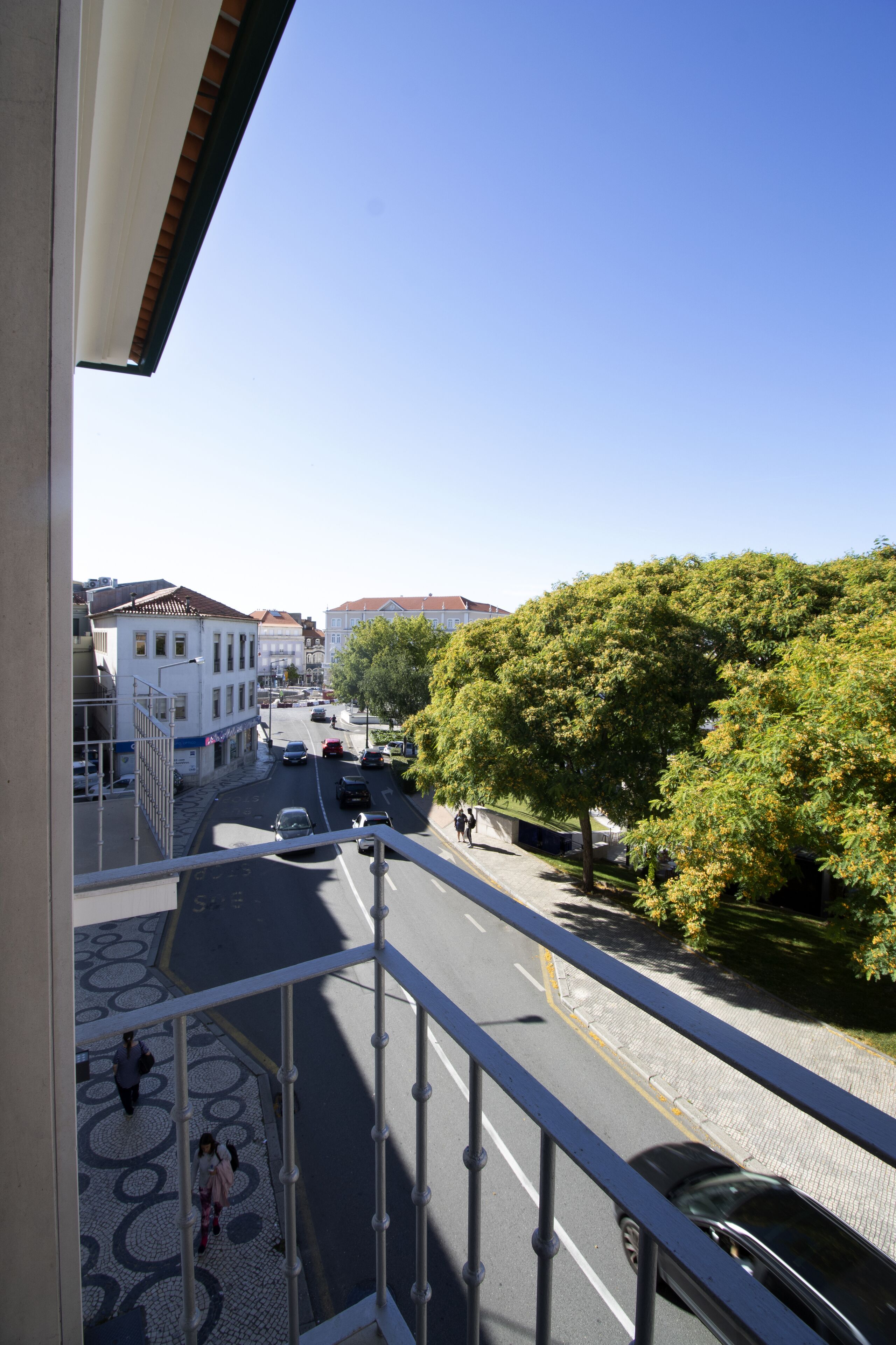 Un balcón con vista a una calle, edificios y árboles.