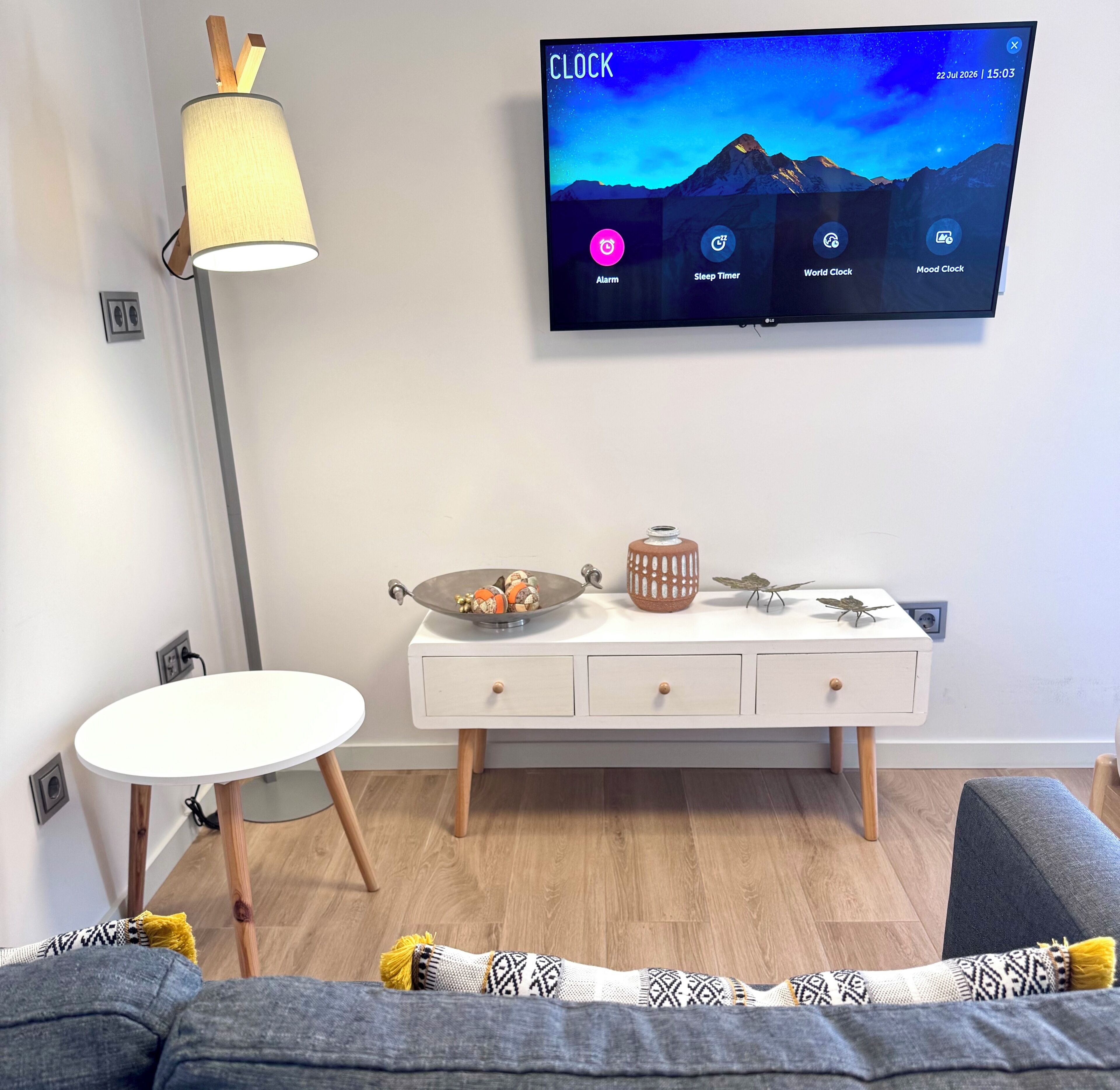 Una sala moderna con televisión de pantalla plana mostrando una aplicación de reloj, una mesa redonda blanca, un sofá y un mueble decorativo.