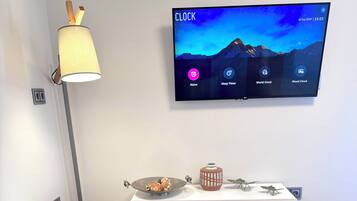 Una sala moderna con televisión de pantalla plana mostrando una aplicación de reloj, una mesa redonda blanca, un sofá y un mueble decorativo.