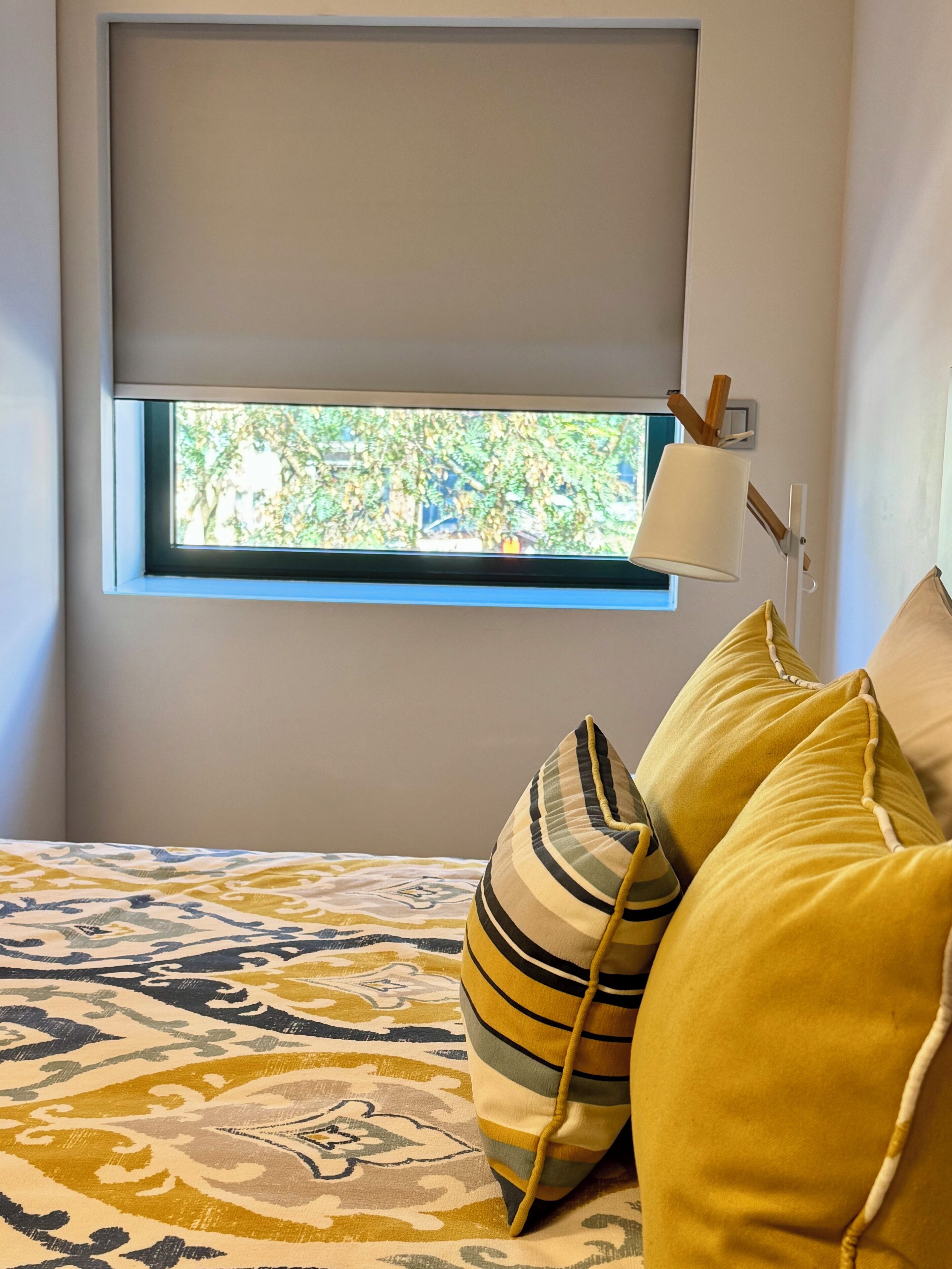 Un dormitorio con cama, ventana con vistas a la vegetación y una lámpara de noche.