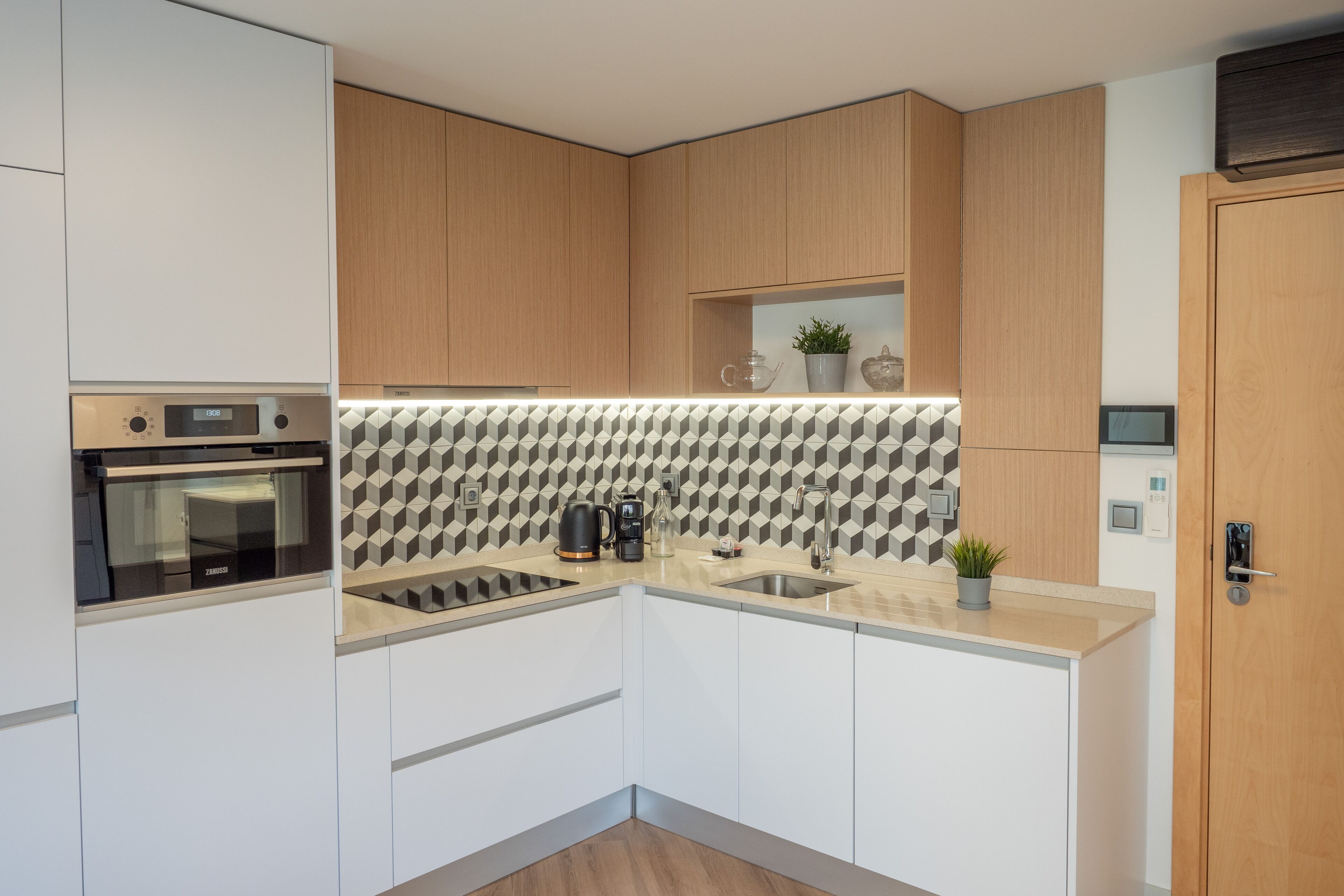 A modern kitchen with white and wooden cabinets, a built-in oven, a sink, and a patterned backsplash.
