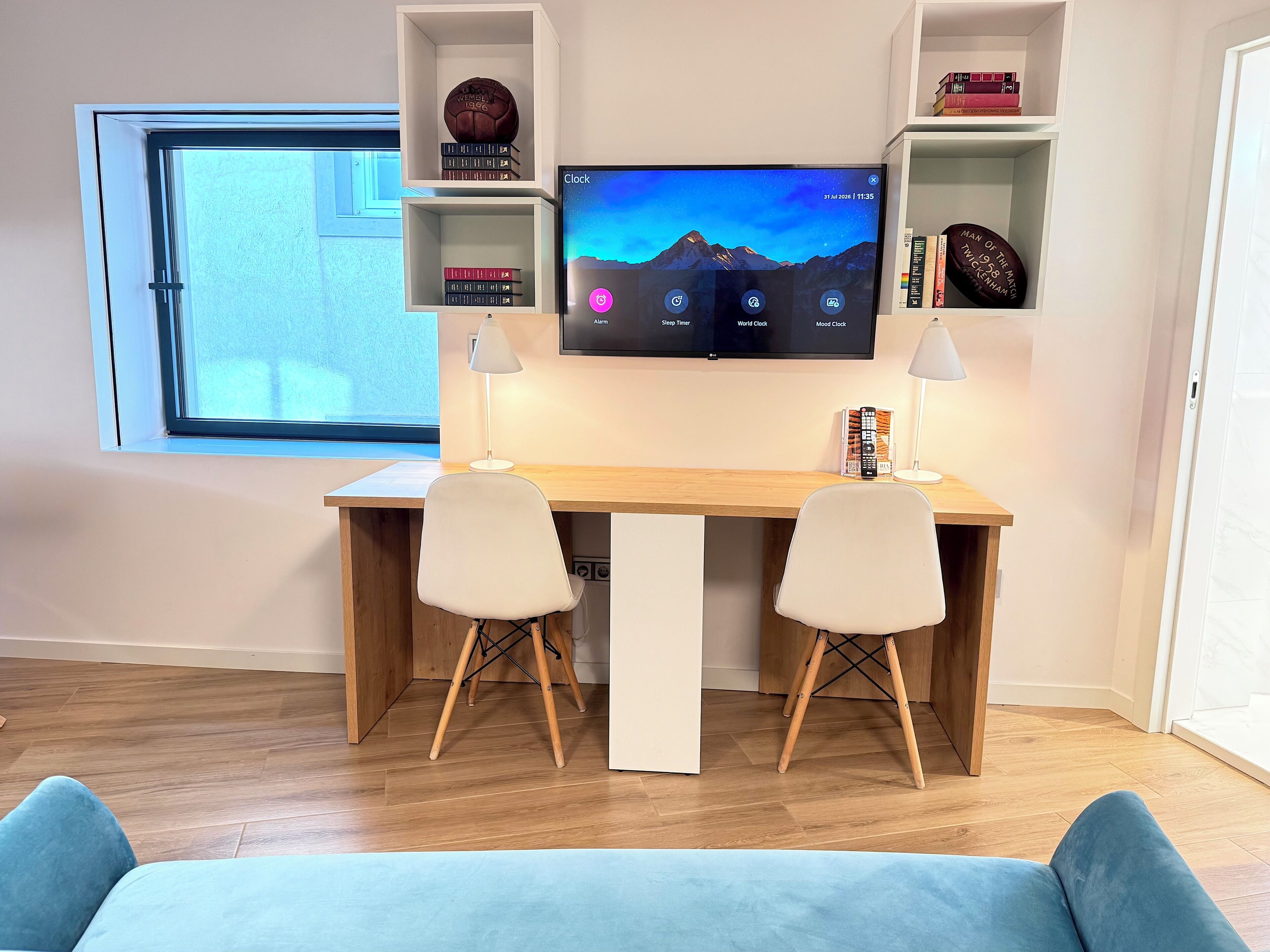 A modern workspace with a desk, two chairs, a TV, and shelves with books and decorative items.
