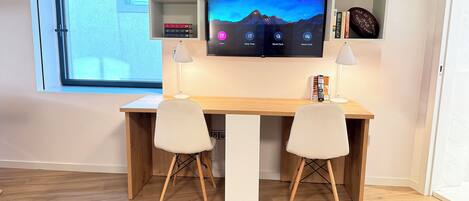 A modern workspace with a desk, two chairs, a TV, and shelves with books and decorative items.