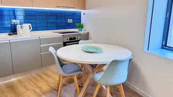 A modern kitchen with a round dining table, two chairs, a coffee maker, and a potted plant.