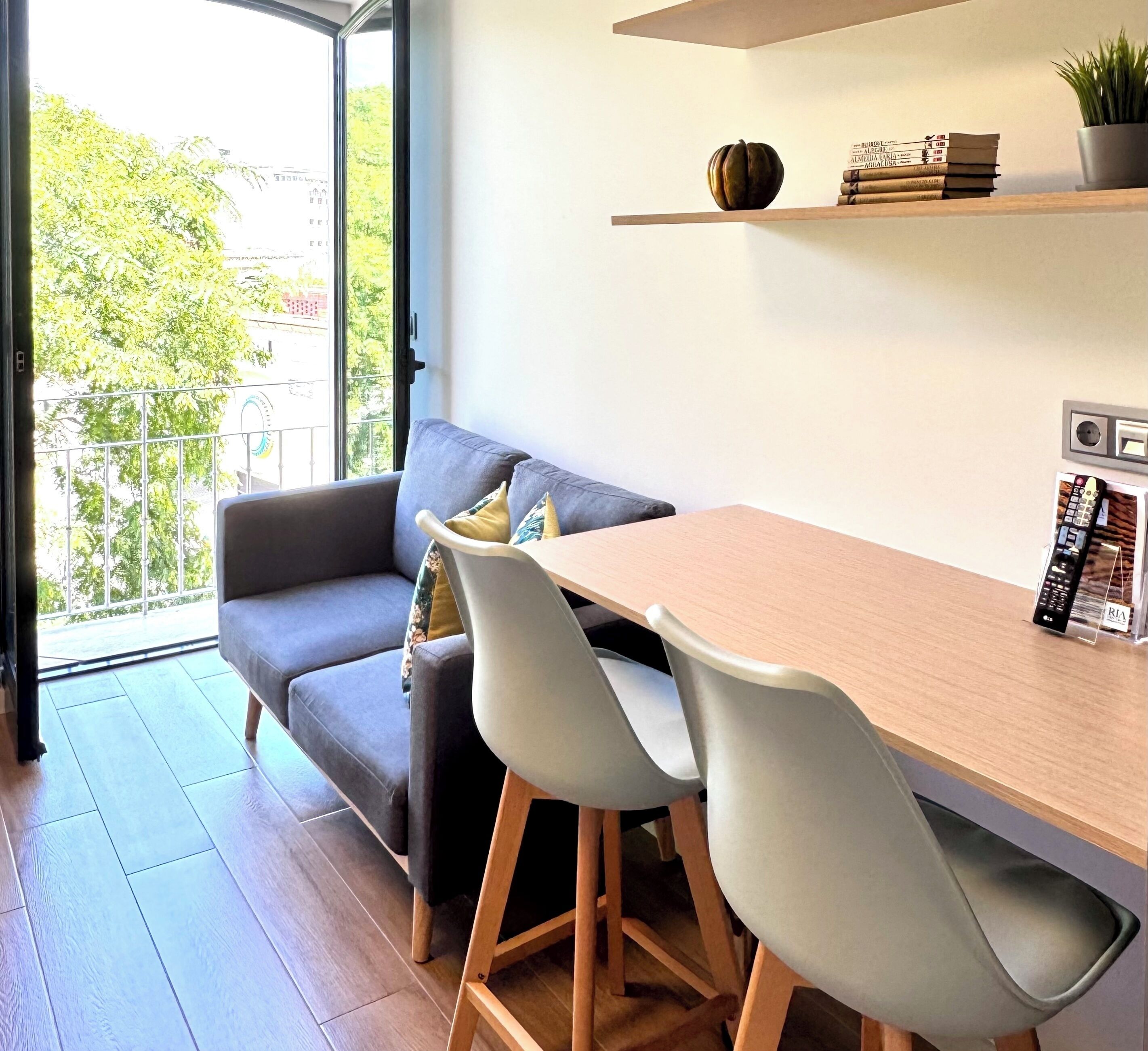 A modern living space with a sofa, two chairs, a wooden table, and a small shelf with books and a plant.