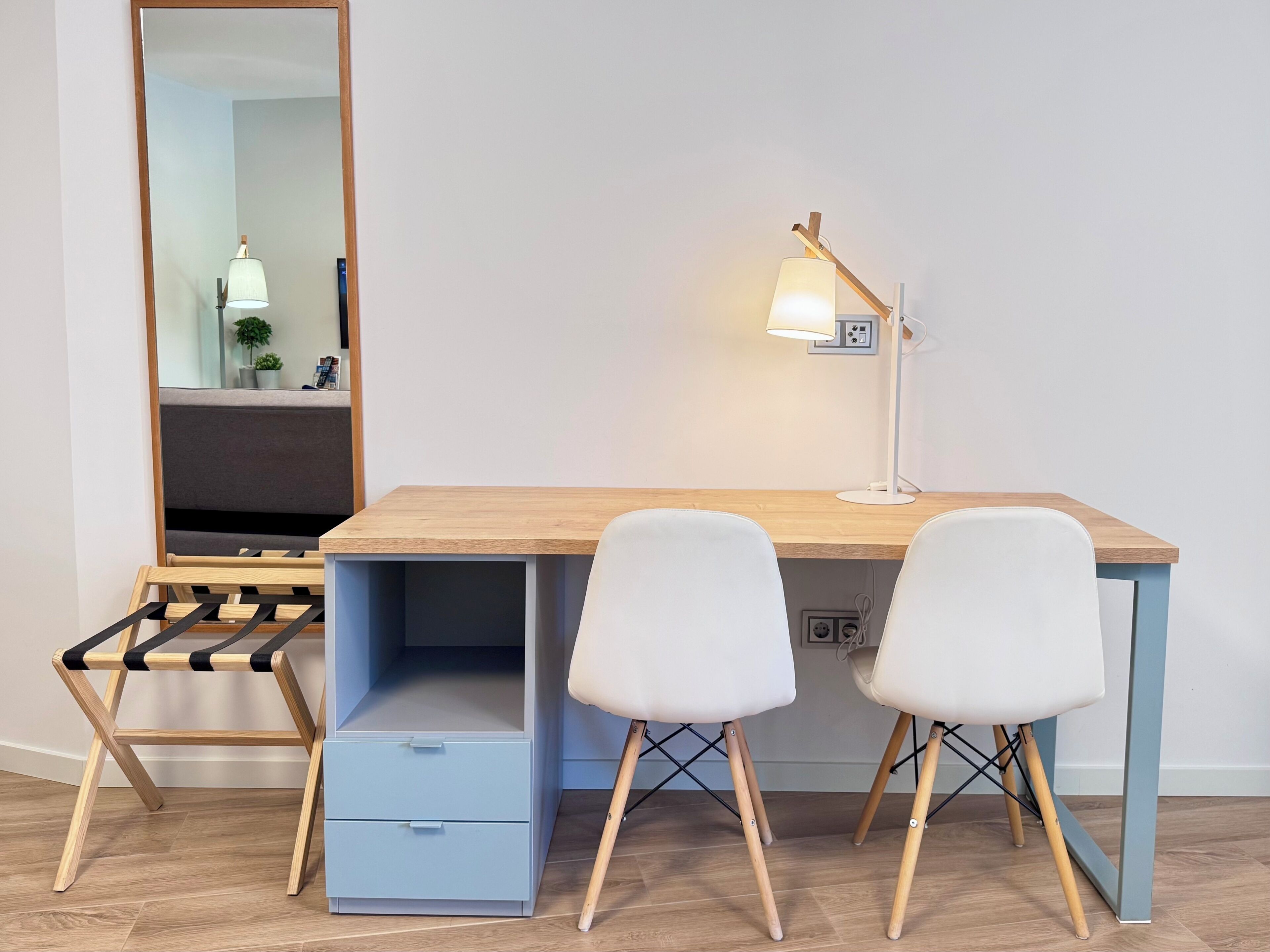A modern study area with a wooden desk, two white chairs, a lamp, and a mirror.