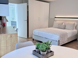 Un dormitorio moderno con cama, mesitas de noche, un escritorio y una planta en maceta.