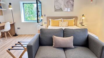 Een moderne slaapkamer met een bed, een grijze bank, een bureau en een televisie.
