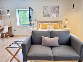 Un dormitorio moderno con cama, un sofá gris, un escritorio y un televisor.