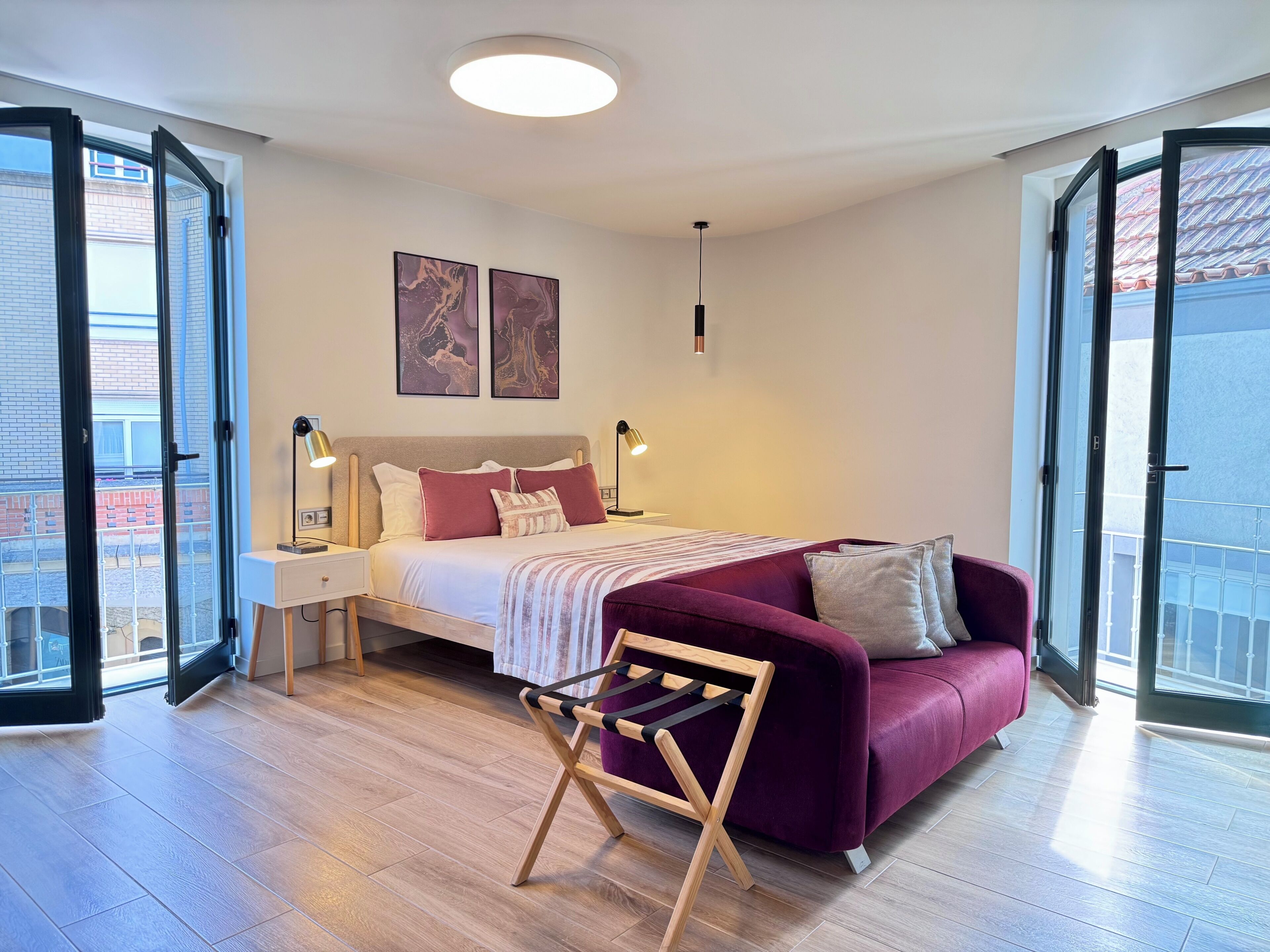 Une chambre moderne avec un lit, des lampes de chevet, un canapé et une vue dégagée grâce à de grandes fenêtres.