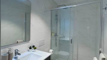 A modern bathroom with a glass shower enclosure, a white sink with a mirror above it, and a toilet.