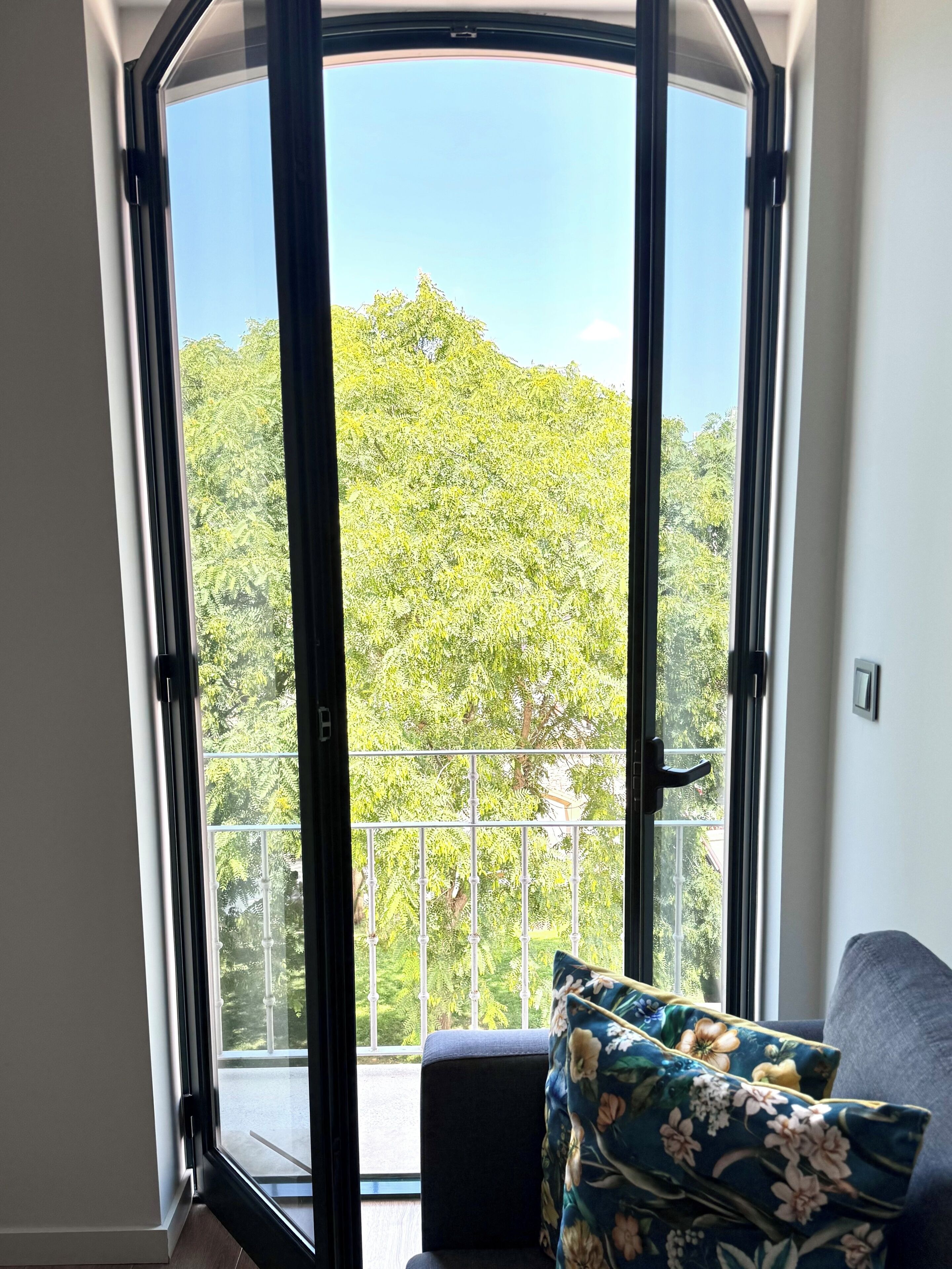 A room with a large window, a sofa with floral cushions, and a view of a green landscape.