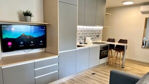 Une cuisine moderne dotée d’un téléviseur encastré, de meubles de rangement gris et d’un coin repas avec une table et des chaises.