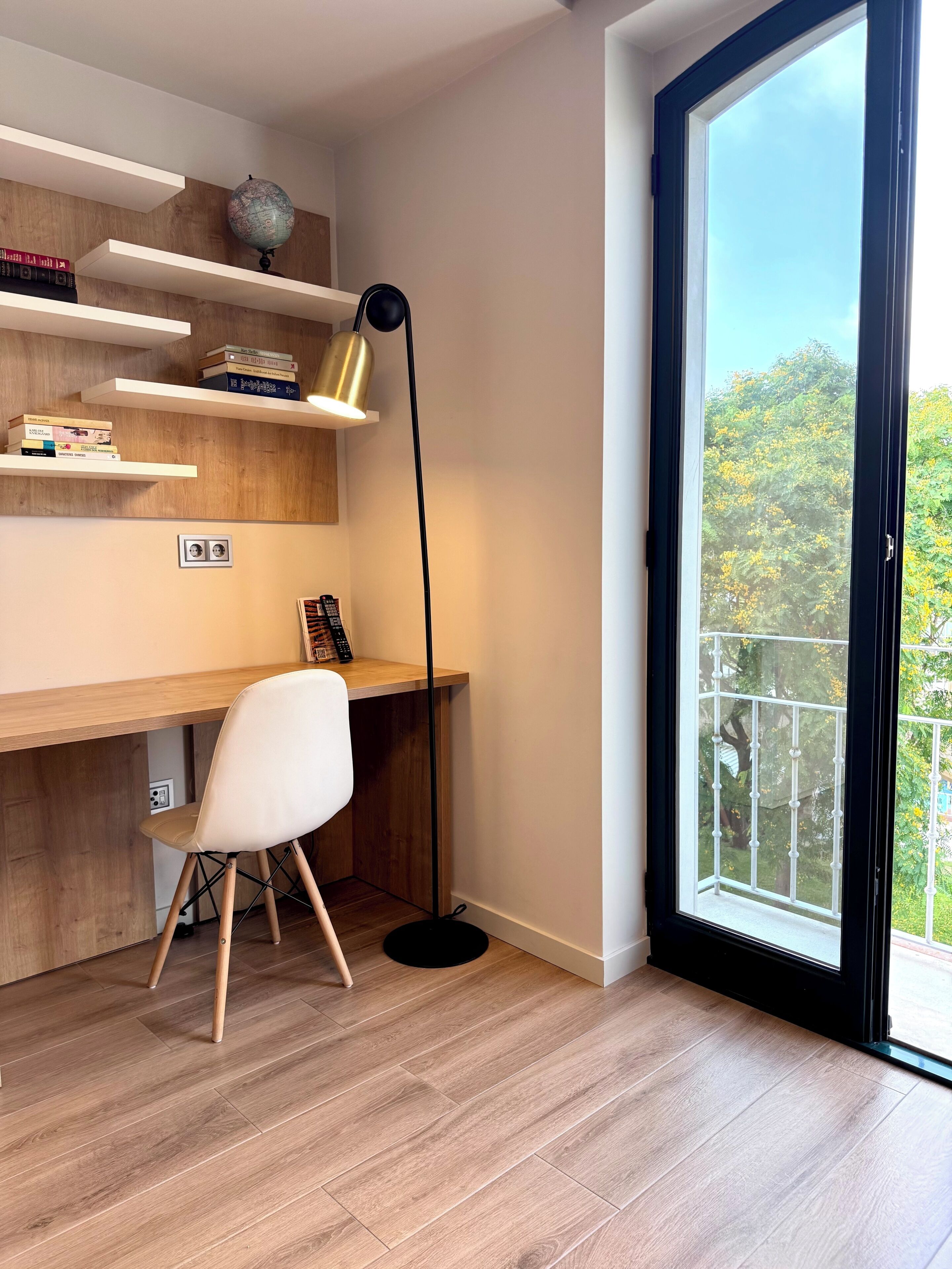 Ein moderner Arbeitsplatz mit Schreibtisch aus Holz, weißem Stuhl und einem Globus auf einem Regal.