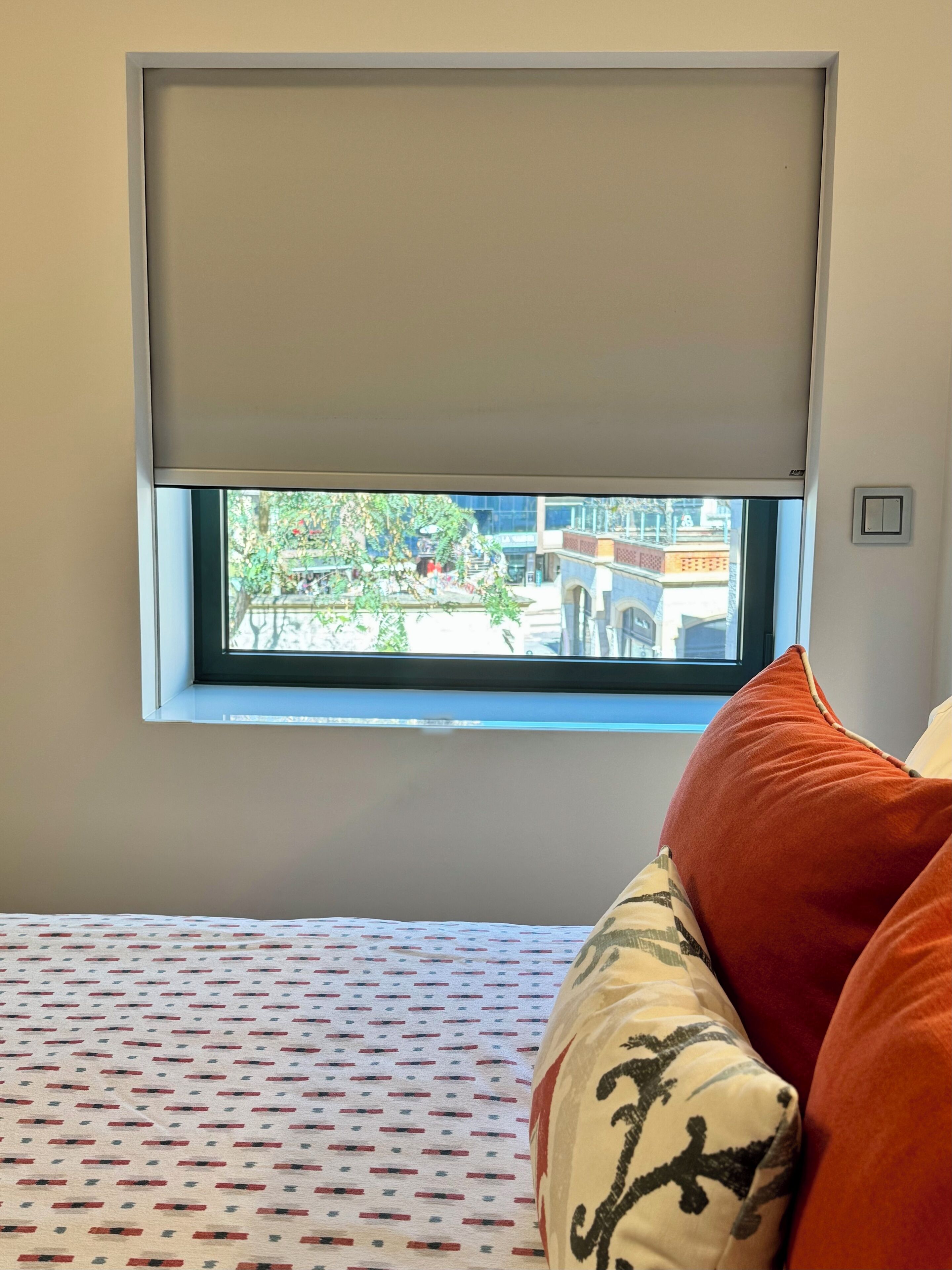 A bedroom with a window, a patterned bedspread, and a pillow with a design.