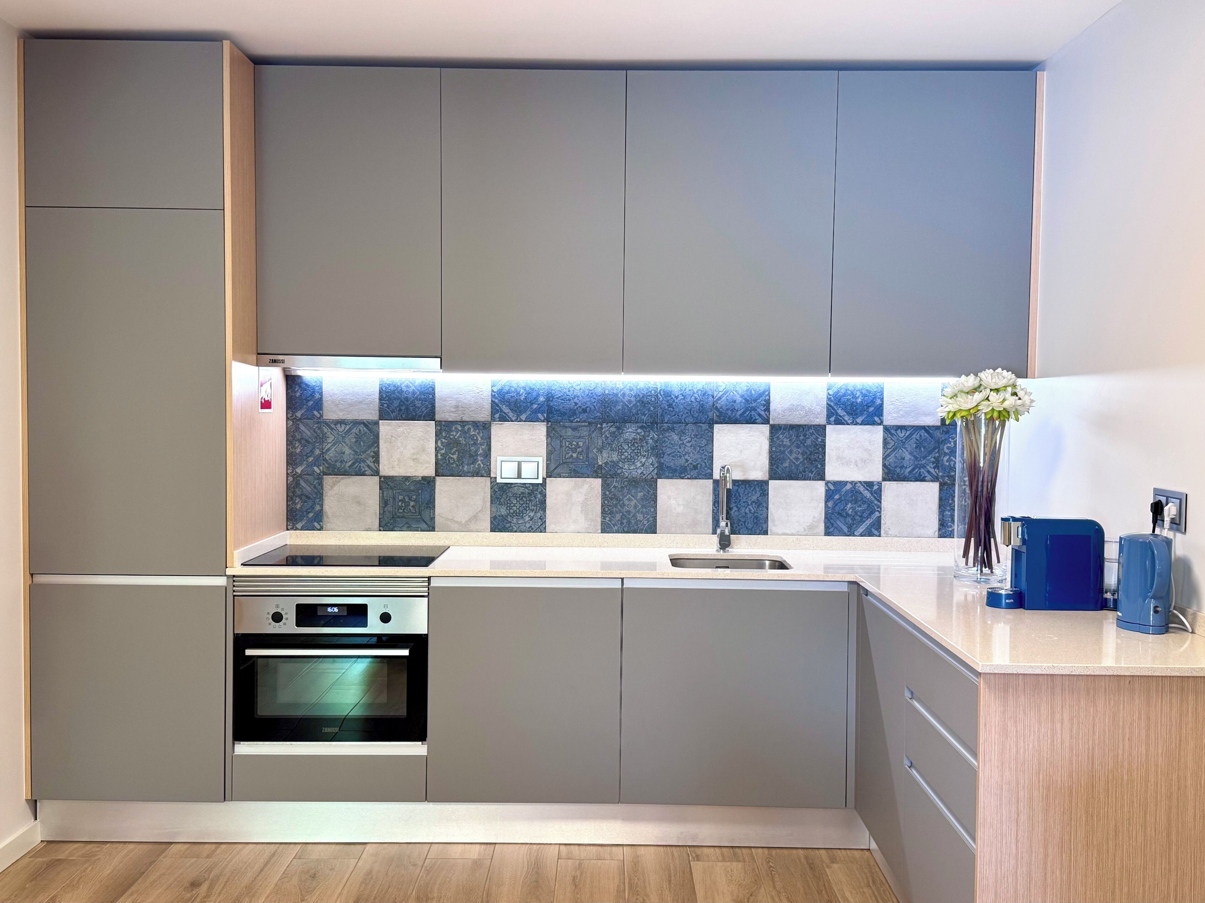 Uma cozinha moderna com armários cinza, uma moldura de backsplash estampada, forno embutido e pia.