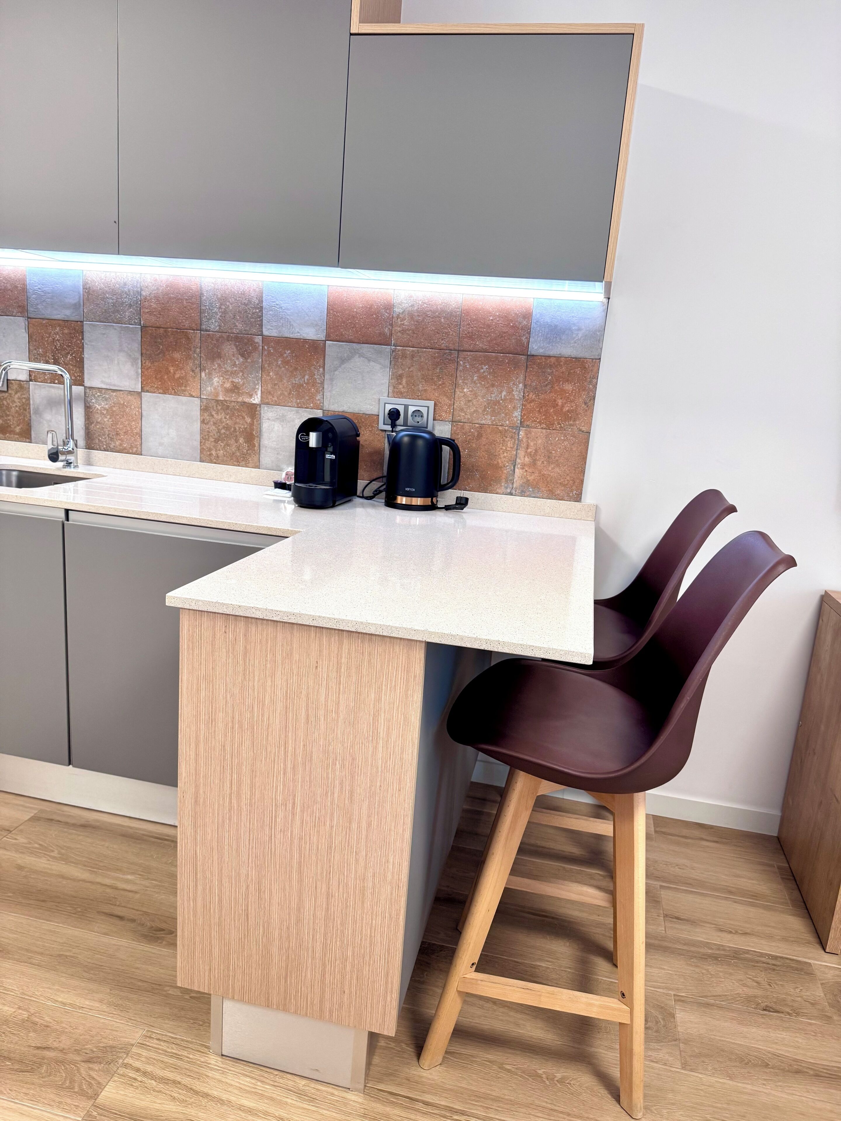 Una cocina compacta con una encimera, una cafetera y una silla.