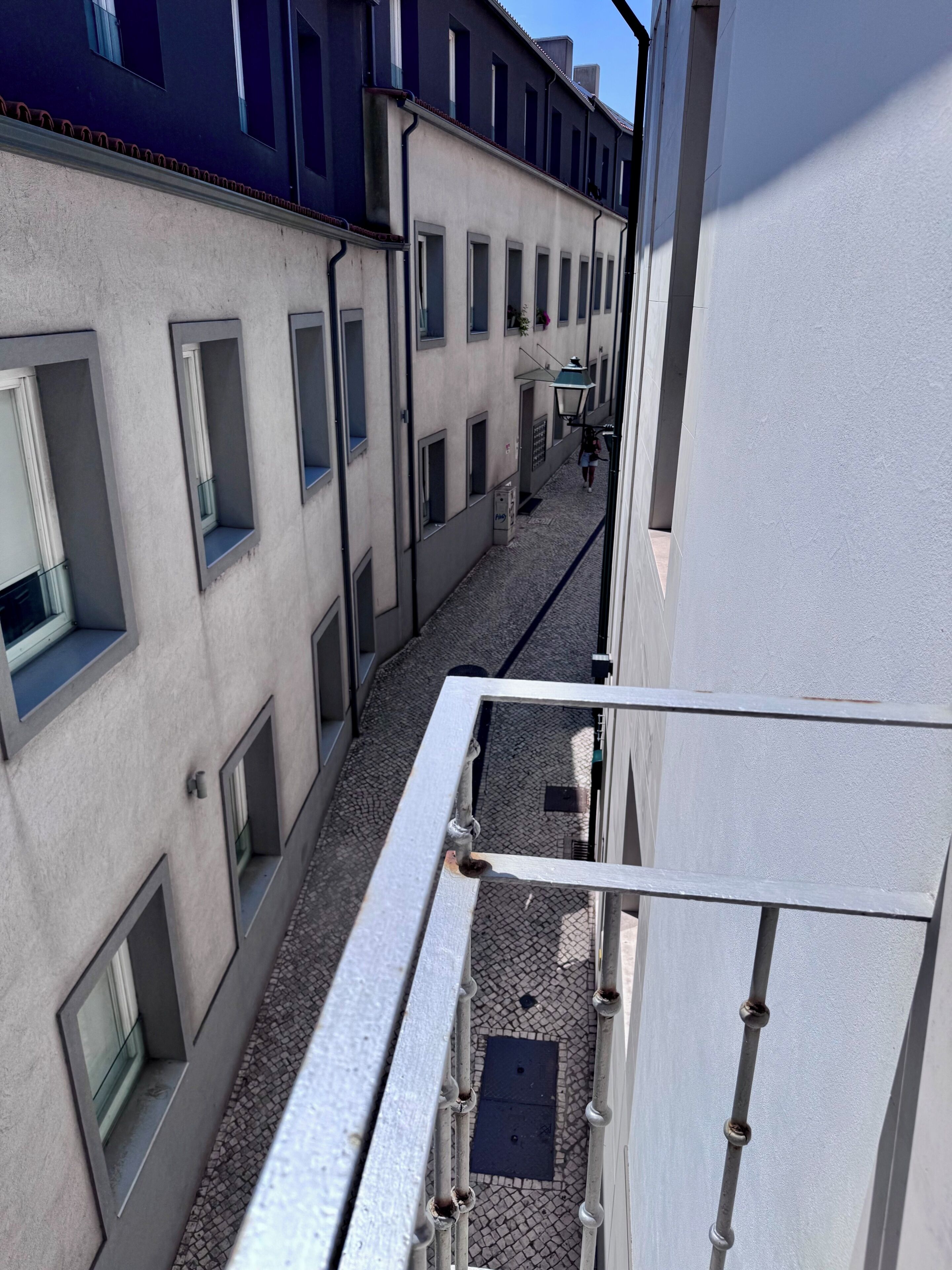 A narrow alleyway between buildings with a metal railing on one side.