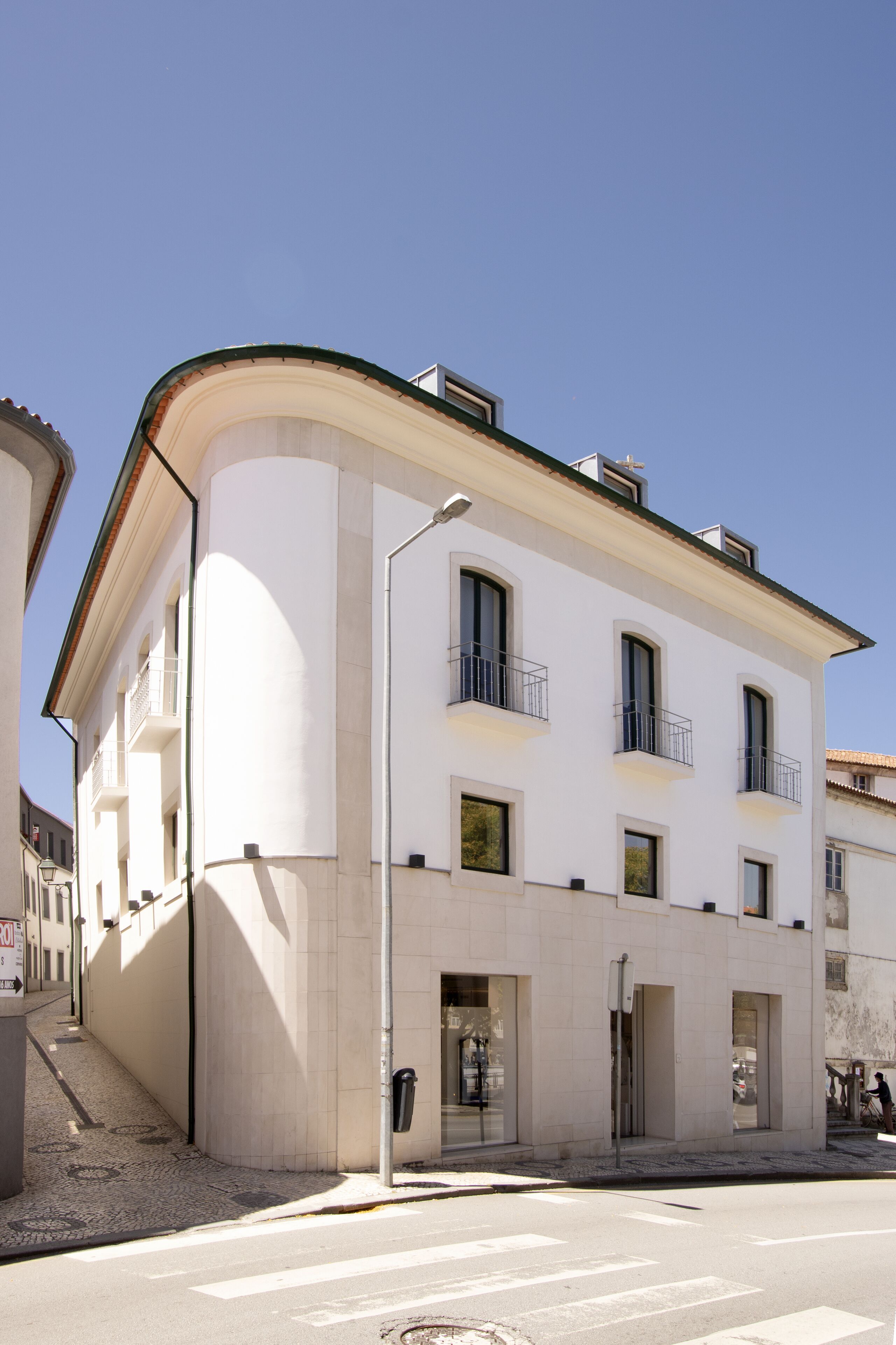 A white building with a curved facade, multiple balconies, and a ground-floor entrance.