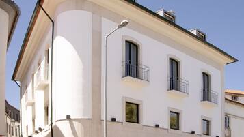 A white building with a curved facade, multiple balconies, and a ground-floor entrance.