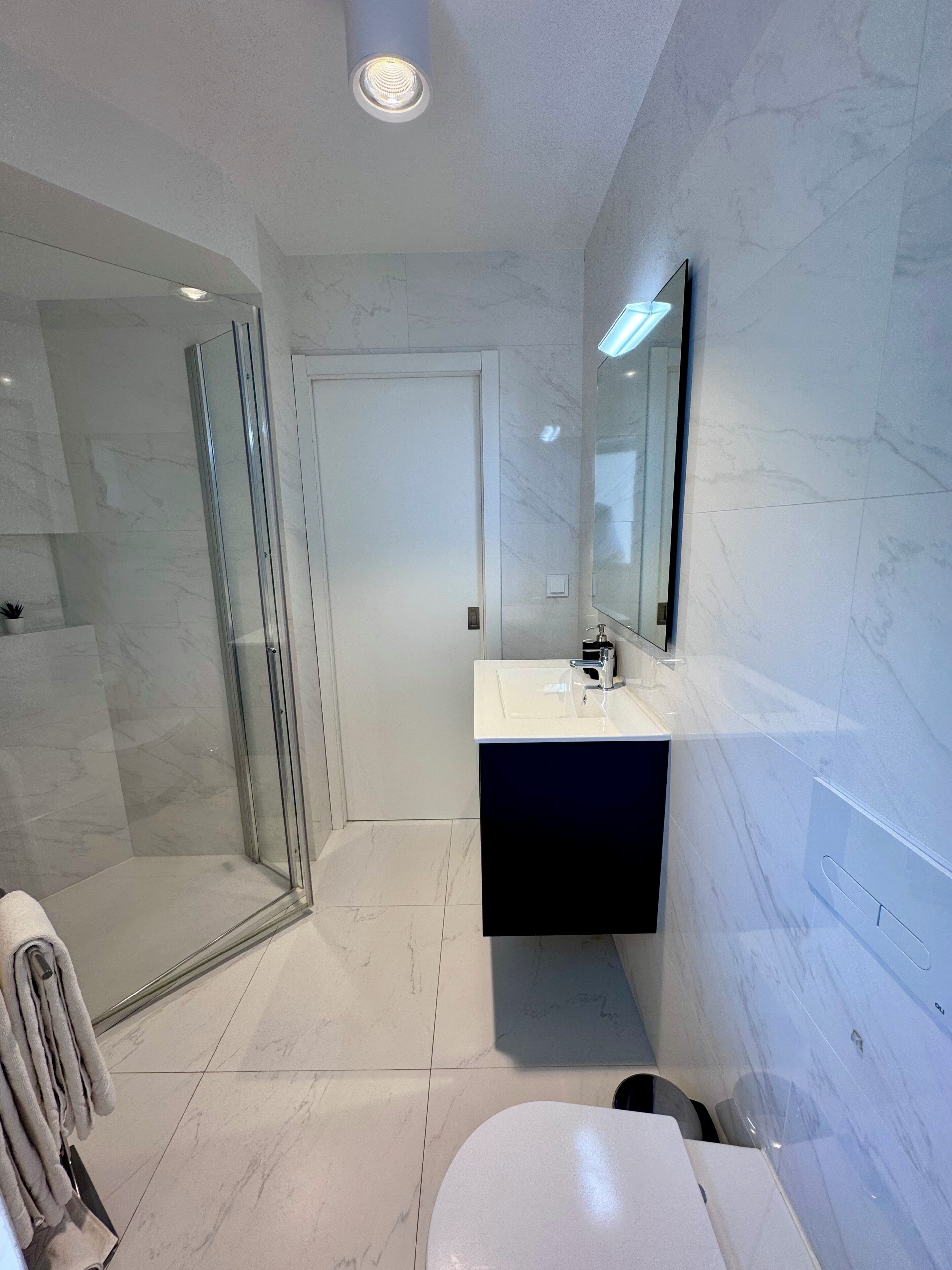 A modern bathroom with a glass shower enclosure, a white sink with a dark cabinet, and a large mirror.